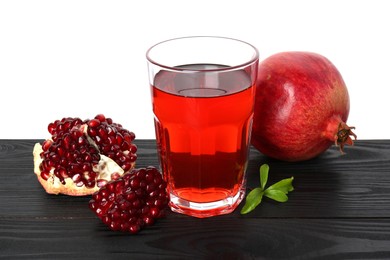 Photo of Refreshing pomegranate juice in glass, leaves and fruits on black wooden table against white background