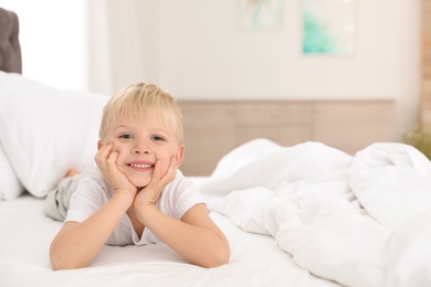 Photo of Cute little boy lying on bed at home. Space for text