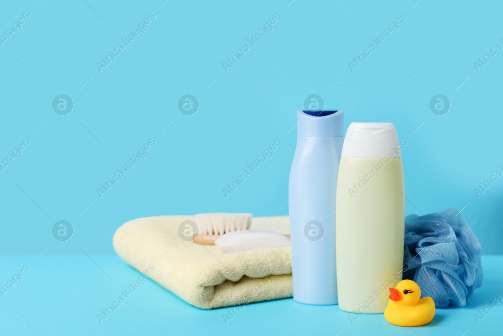 Photo of Baby cosmetic products, bath duck, accessories and towel on light blue background. Space for text