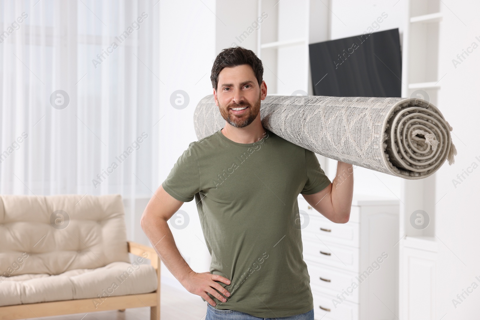 Photo of Smiling man holding rolled carpet in room