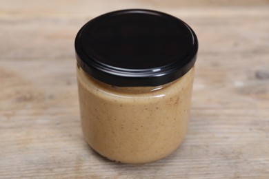 Photo of Tasty nut paste in jar on wooden table, closeup