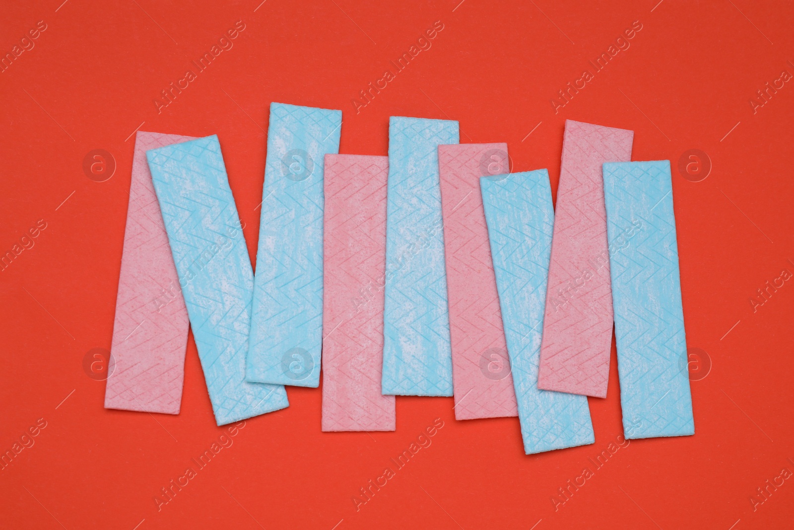 Photo of Sticks of tasty chewing gum on red background, flat lay