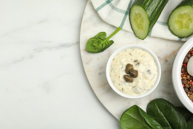 Creamy caper sauce in bowl and ingredients on white marble table, flat lay. Space for text