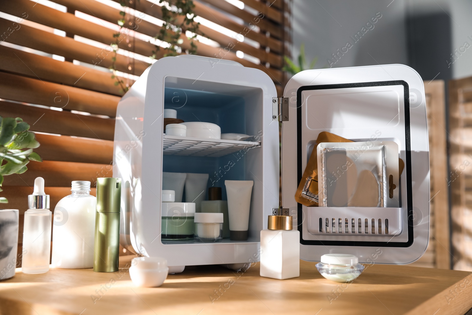 Photo of Mini fridge with cosmetic products on wooden vanity table