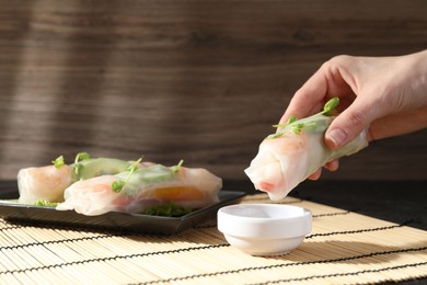 Photo of Woman dipping delicious spring roll into sauce at table, closeup