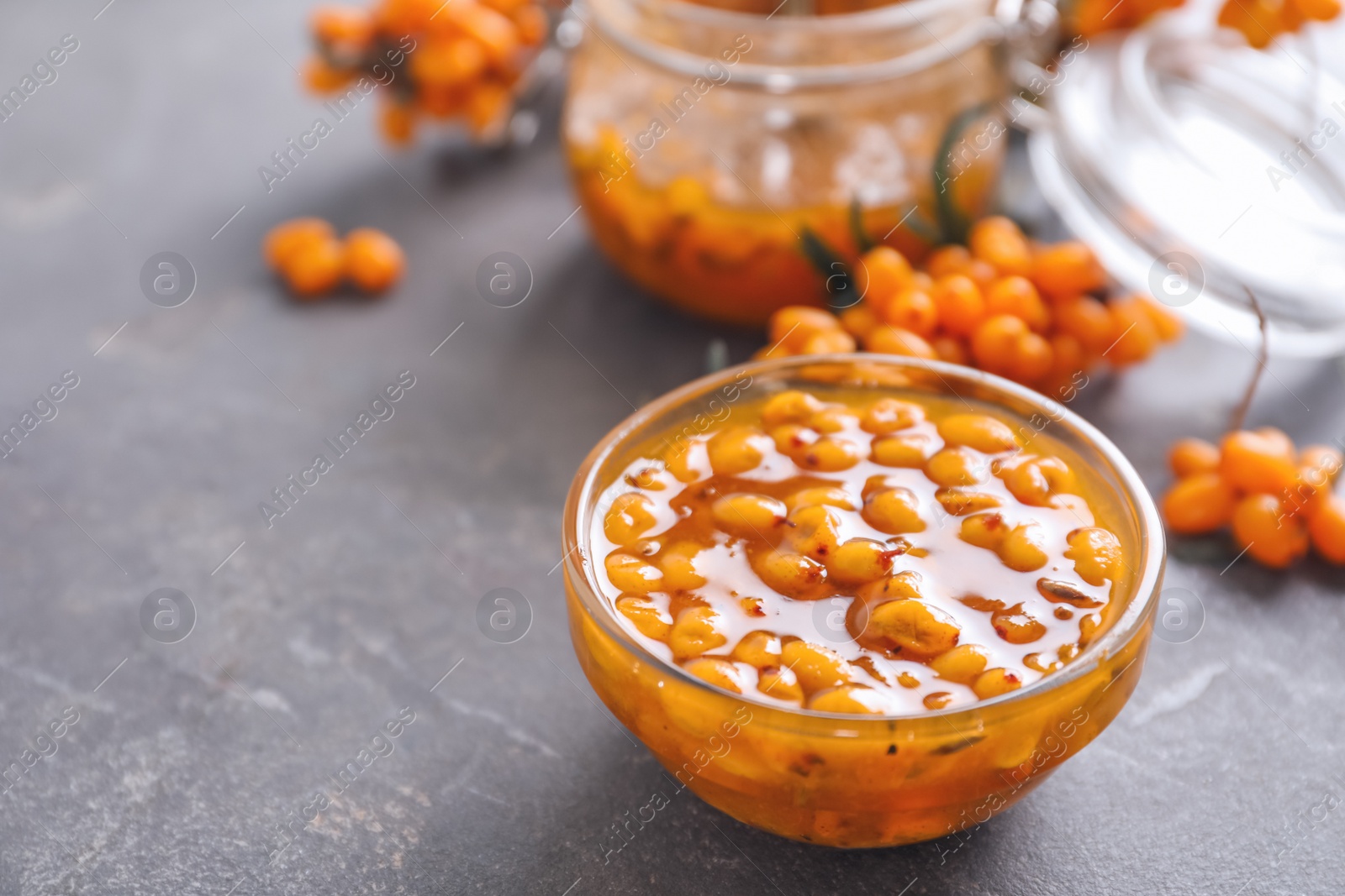 Photo of Delicious sea buckthorn jam and fresh berries on grey table. Space for text