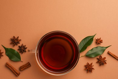 Cup of tea, anise stars, green leaves and cinnamon sticks on brown background, flat lay. Space for text