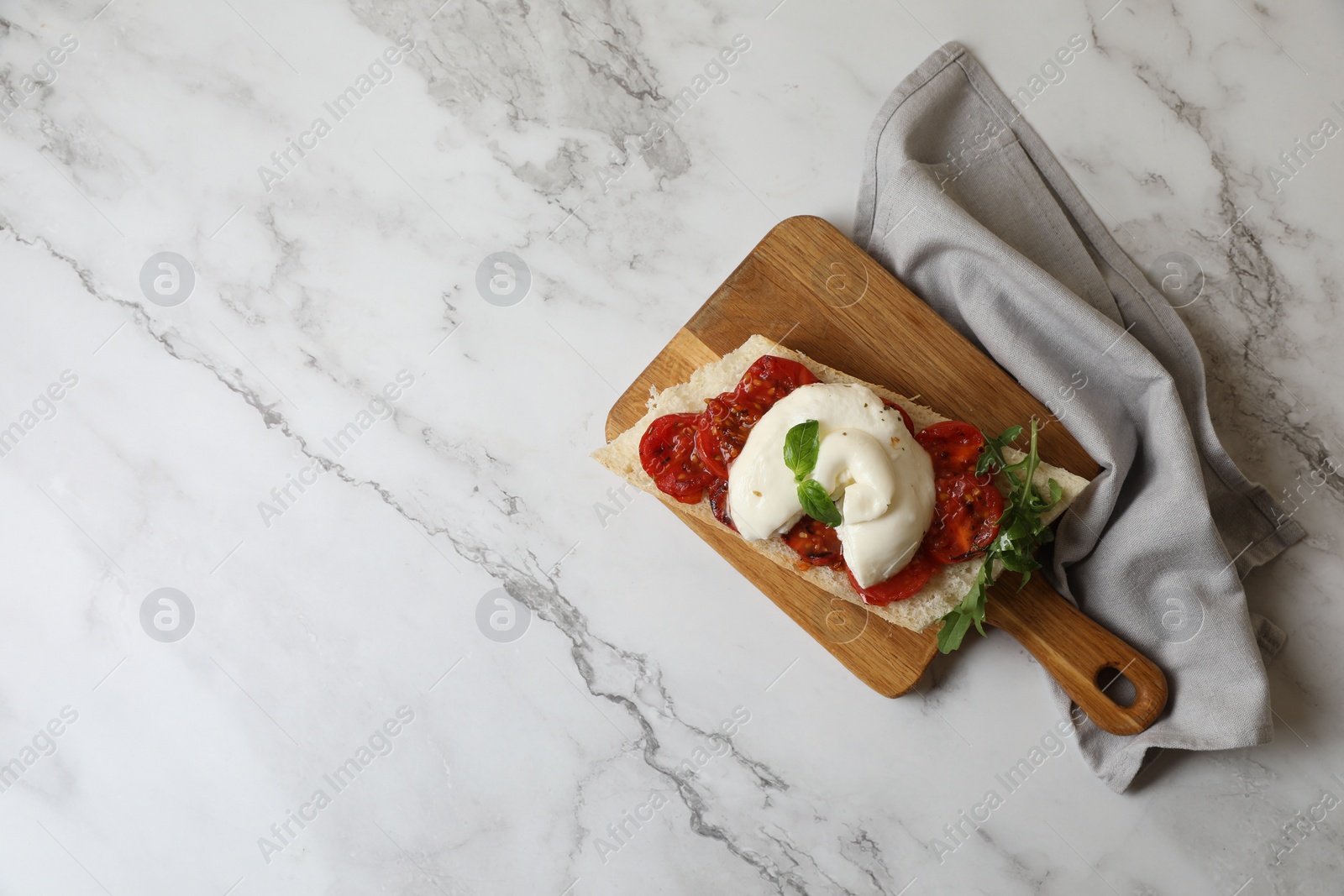 Photo of Toast with delicious burrata cheese, tomatoes and arugula on white marble table, top view. Space for text