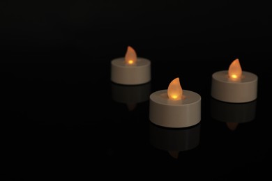 Photo of Glowing decorative LED candles on black background. Space for text