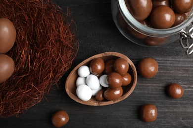 Photo of Half of tasty chocolate egg, decorative nest and candies on black wooden table, flat lay