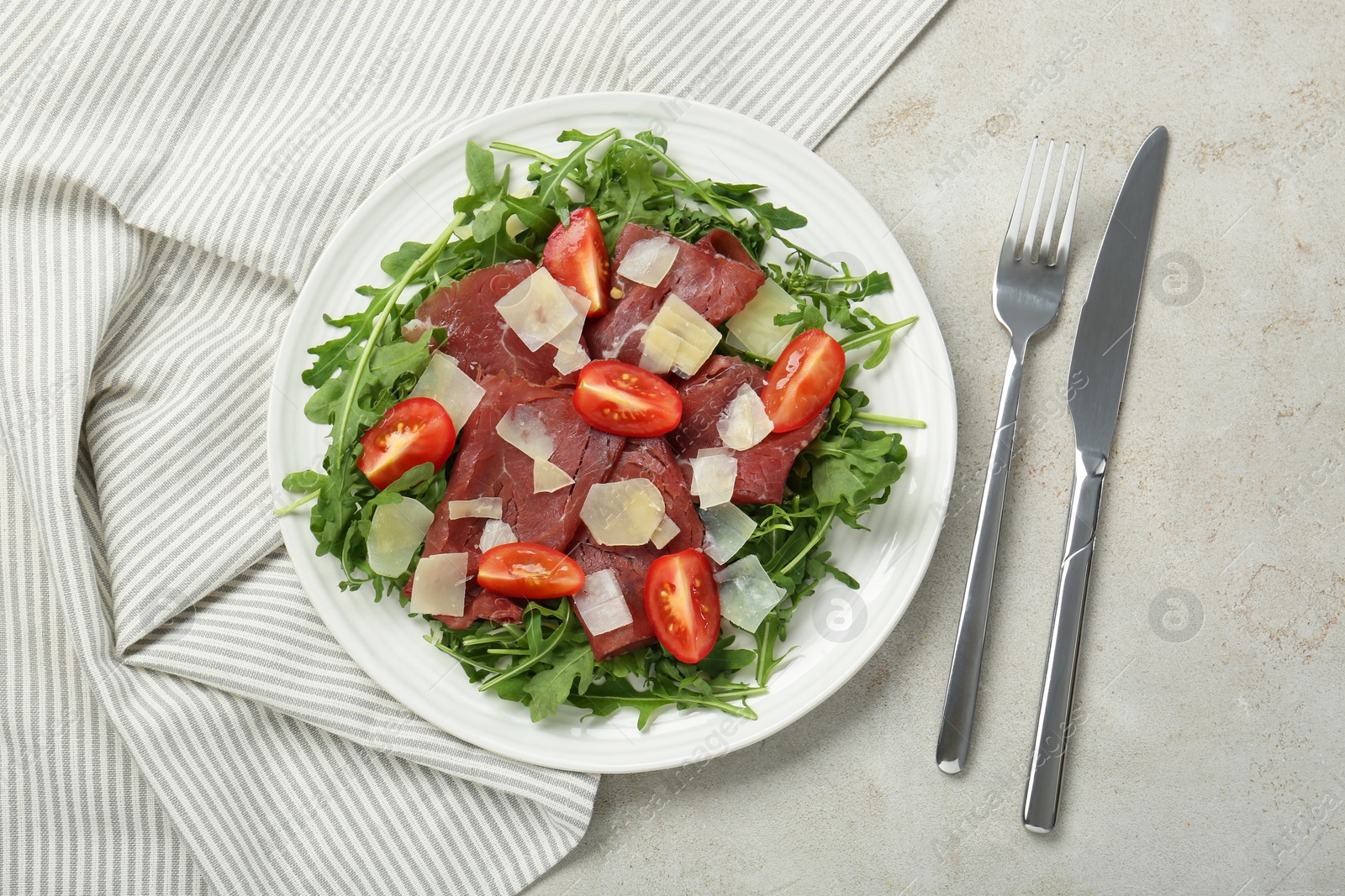 Photo of Delicious bresaola salad with parmesan cheese served on light grey textured table, flat lay