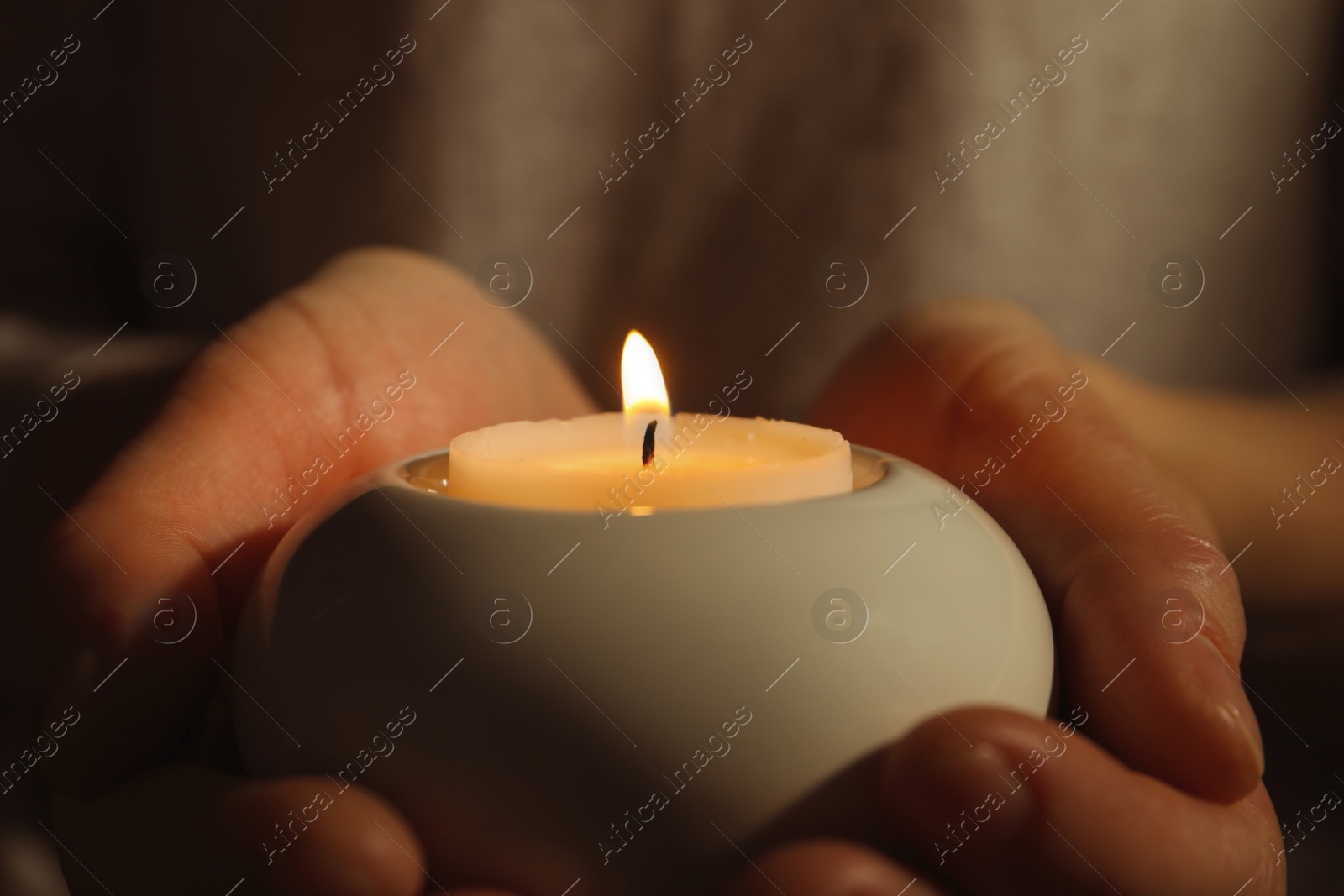 Photo of Young person holding burning candle in darkness, closeup