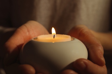 Photo of Young person holding burning candle in darkness, closeup