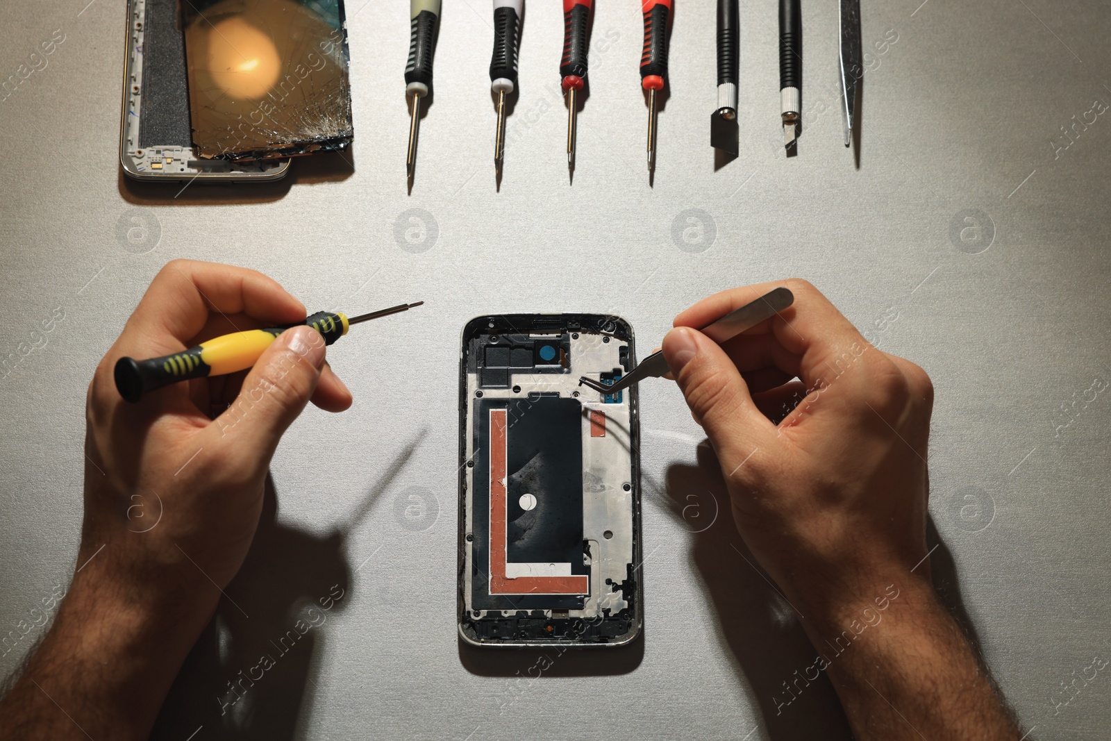Photo of Man repairing broken smartphone at light grey table, top view
