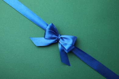 Blue satin ribbon with bow on green background, top view