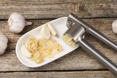 Garlic press, cloves and mince on wooden table, top view