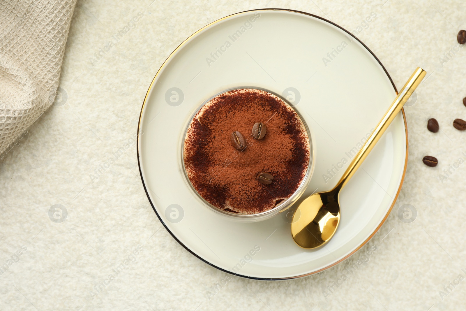 Photo of Delicious tiramisu in glass, coffee beans and spoon on white table, top view