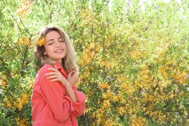 Attractive young woman posing near blossoming bush on sunny spring day