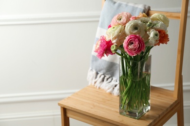 Photo of Beautiful ranunculus flowers in vase on wooden chair indoors, space for text
