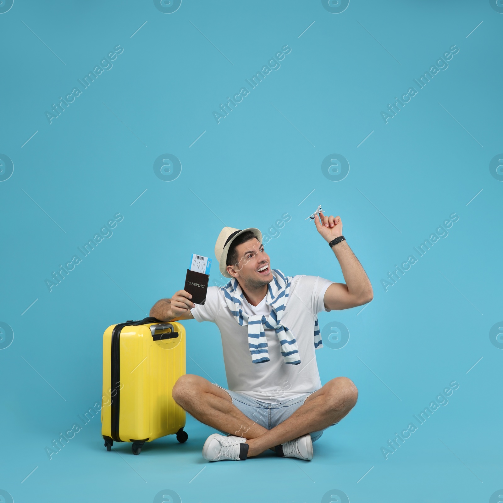 Photo of Male tourist holding passport with ticket and toy airplane near suitcase on turquoise background, space for text