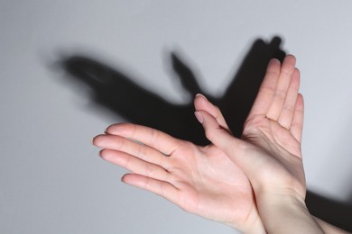 Photo of Shadow puppet. Woman making hand gesture like bird on light background, closeup