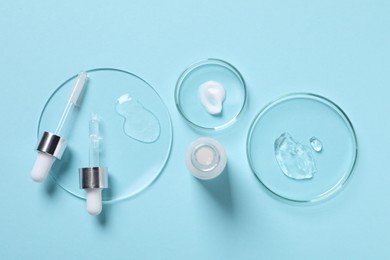 Photo of Petri dishes with samples of cosmetic serums, bottle and pipettes on light blue background, flat lay