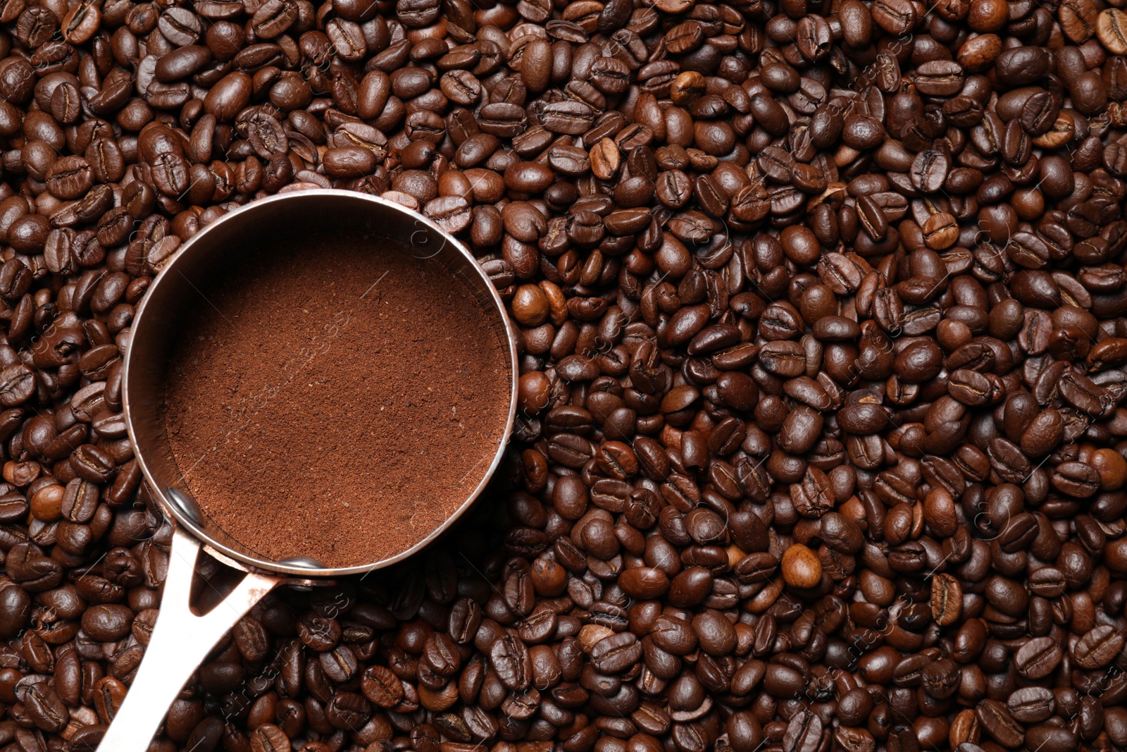 Photo of Pot with ground coffee on roasted beans, top view. Space for text