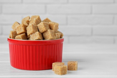 Photo of Brown sugar cubes in bowl on white wooden table, closeup. Space for text