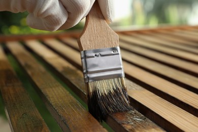 Photo of Worker applying wood stain onto planks outdoors, closeup