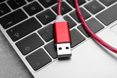 Photo of Red USB cable and laptop on grey table, closeup