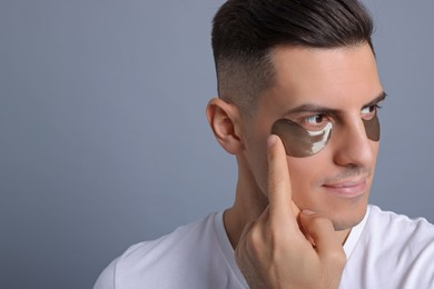 Photo of Man applying dark under eye patch on grey background. Space for text