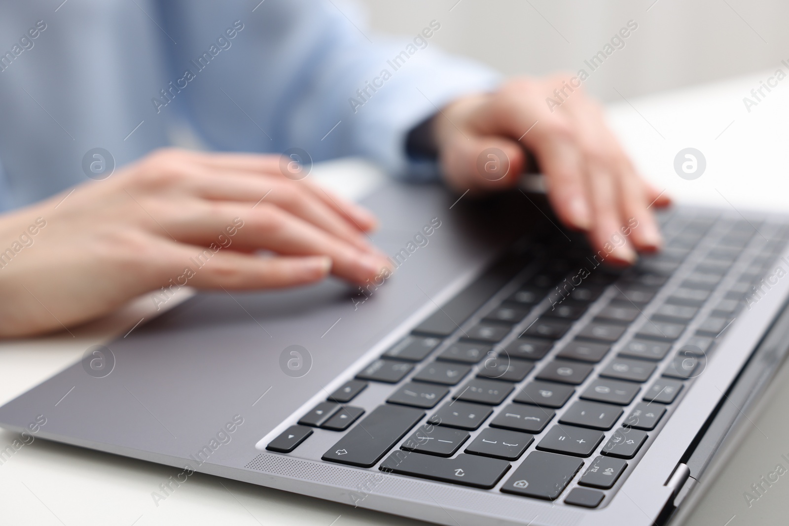 Photo of E-learning. Woman using laptop at white table indoors, closeup