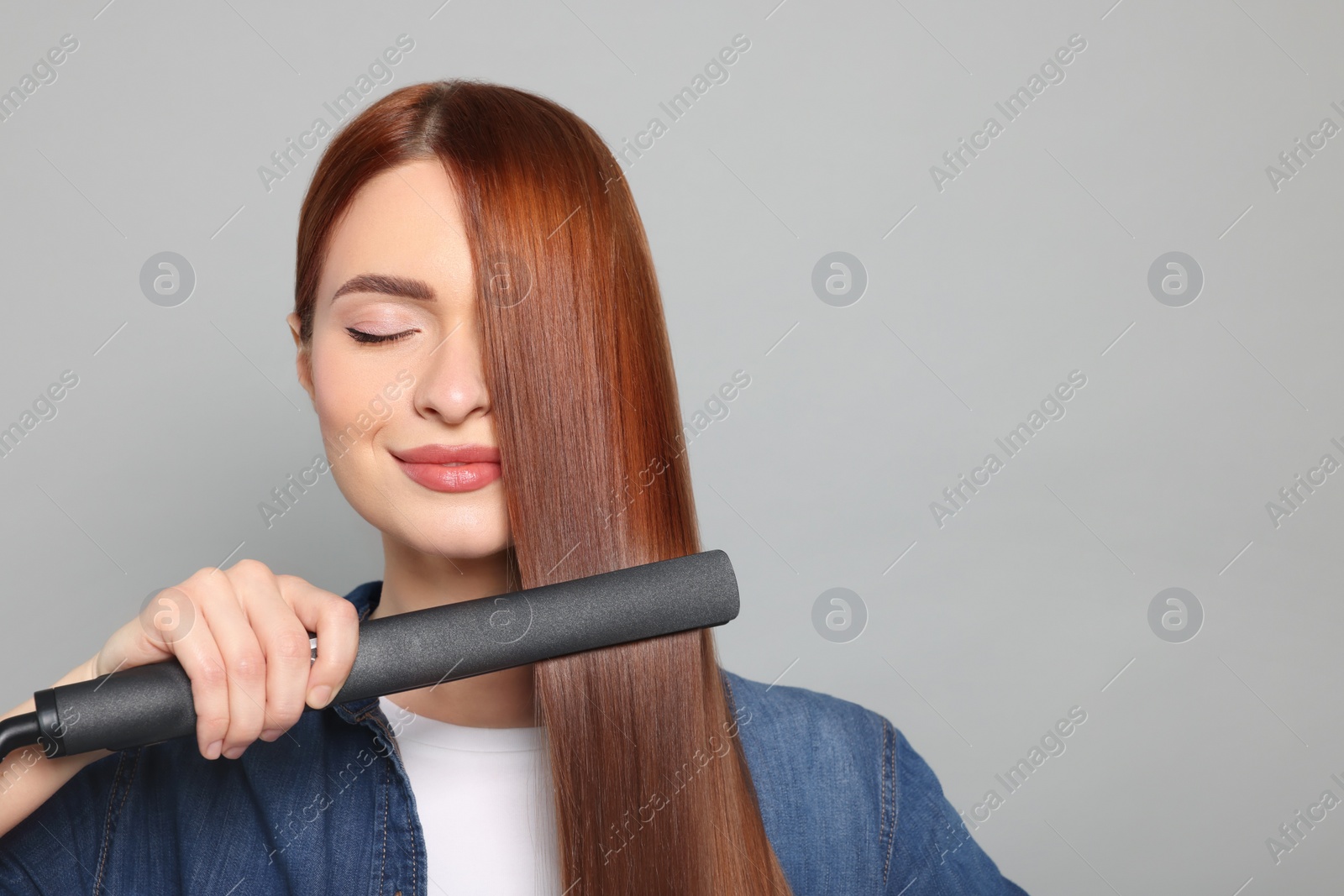 Photo of Beautiful woman using hair iron on light gray background, space for text