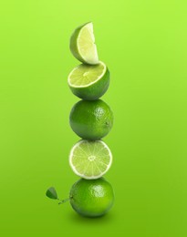 Image of Stacked whole and cut limes on bright green background