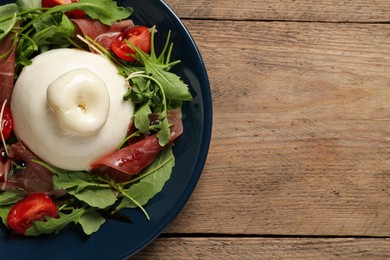 Photo of Delicious burrata salad with tomatoes, prosciutto and arugula on wooden table, top view. Space for text