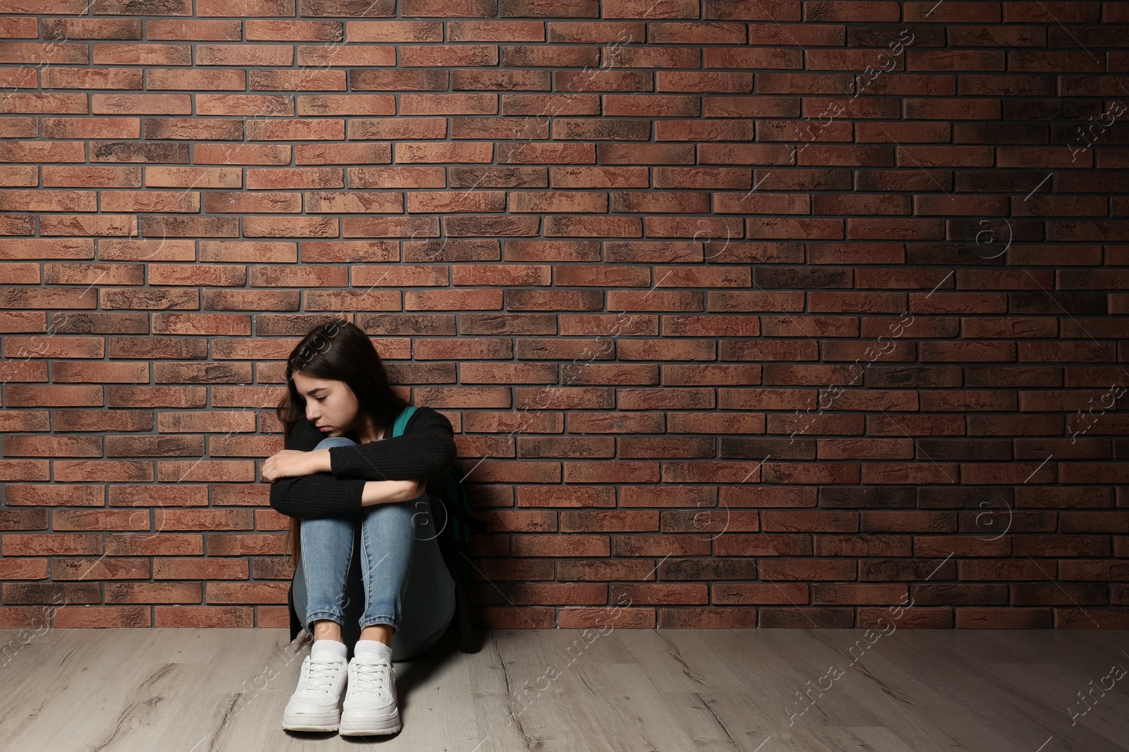 Photo of Upset teenage girl sitting on floor near wall. Space for text