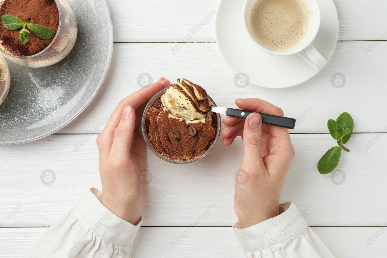 Photo of Woman eating delicious tiramisu at white wooden table, top view