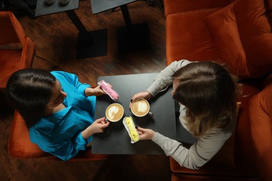 Photo of Young women with coffee and eclairs spending time together in cafe, above view