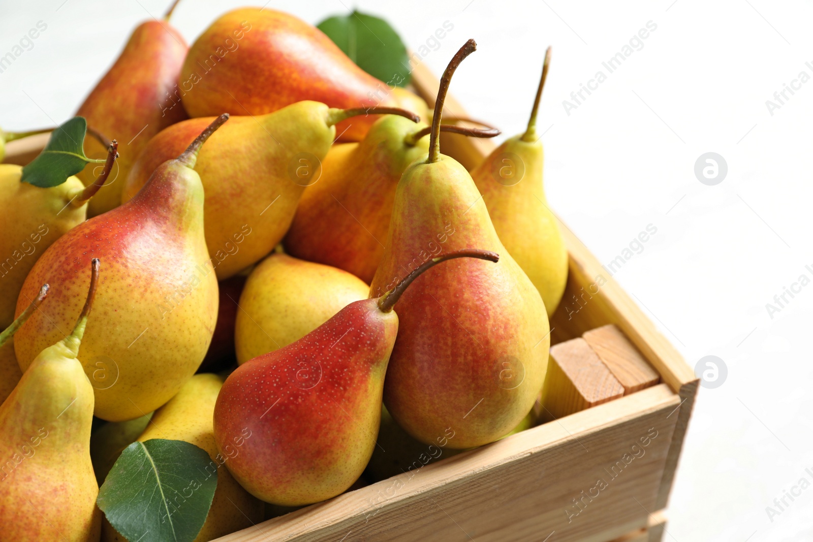 Photo of Wooden crate with ripe pears on light background, closeup