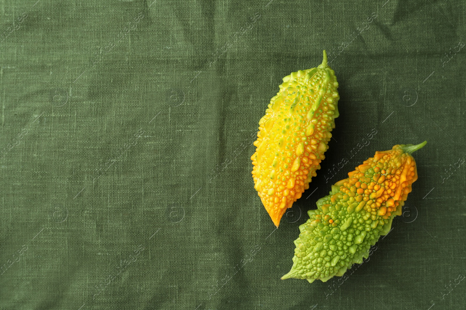 Photo of Fresh bitter melons on dark green cloth, flat lay. Space for text