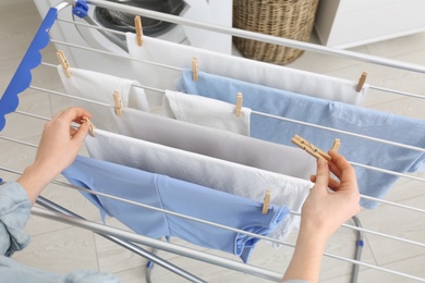 Woman hanging clean laundry on drying rack indoors, closeup