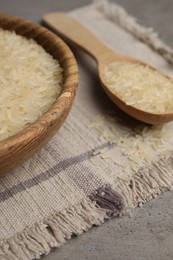 Photo of Bowl and spoon of raw rice on grey table, closeup