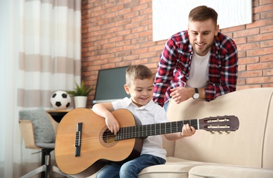 Father watching his son playing guitar at home