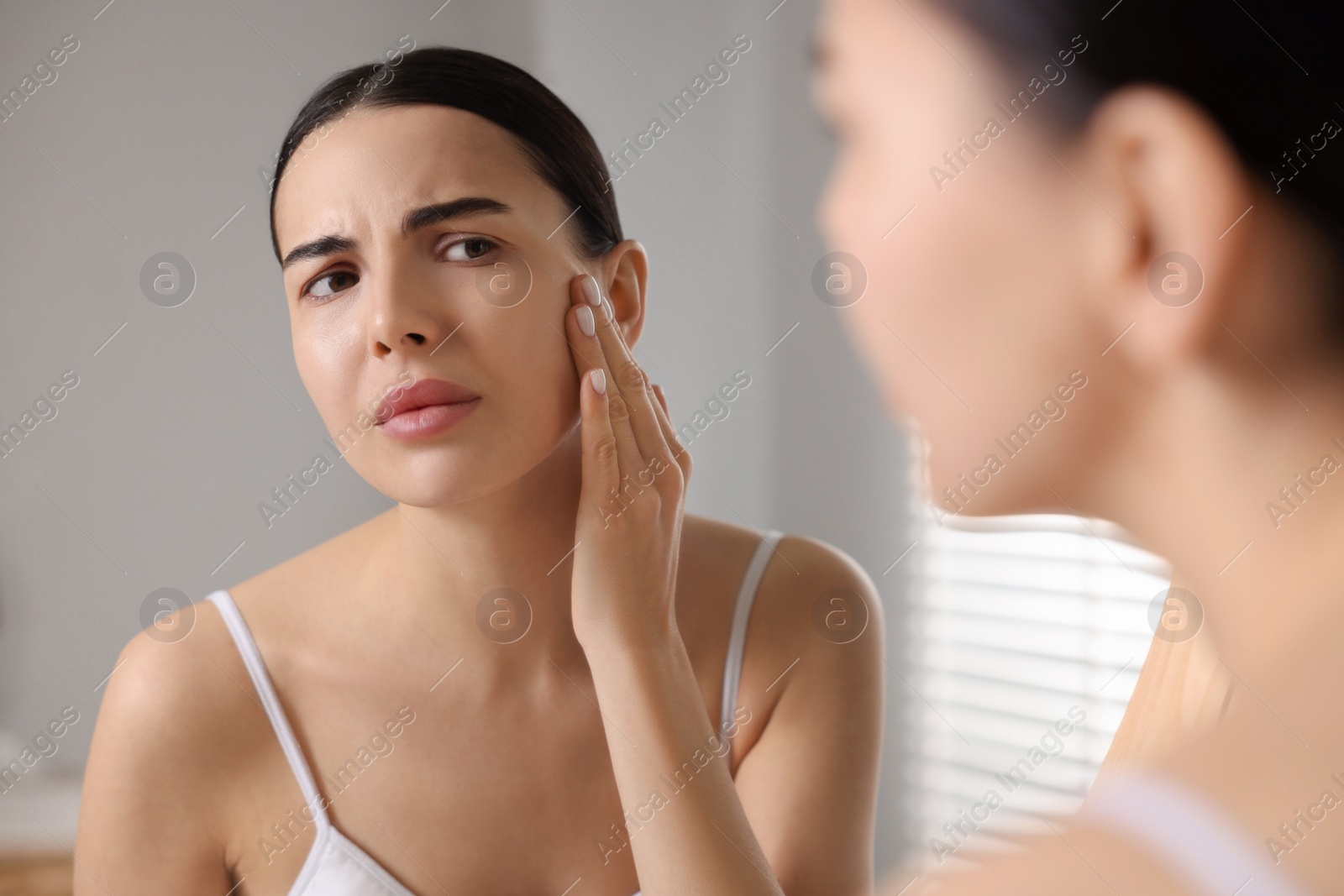 Photo of Woman with dry skin looking at mirror in bathroom