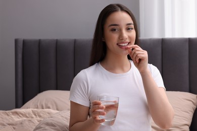 Photo of Beautiful young woman with glass of water taking pill at home, space for text