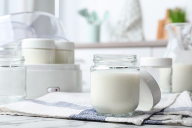 Glass jar with tasty yogurt on white marble table in kitchen