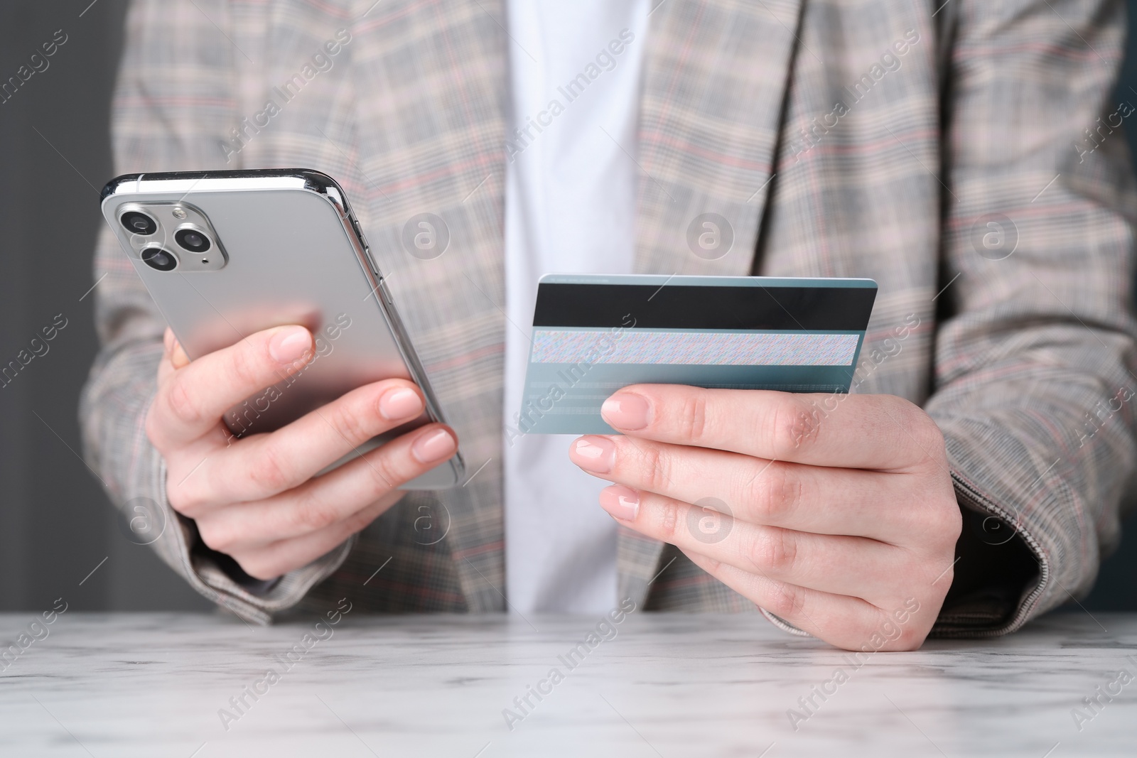 Photo of Online payment. Woman with smartphone and credit card at white marble table, closeup