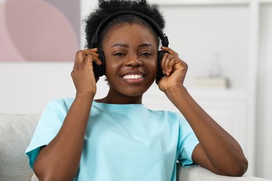 Beautiful young woman in headphones enjoying music on sofa indoors