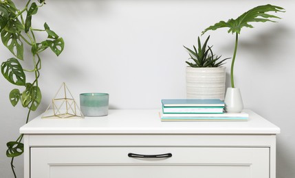 Photo of Chest of drawers with interior accessories and houseplants near white wall