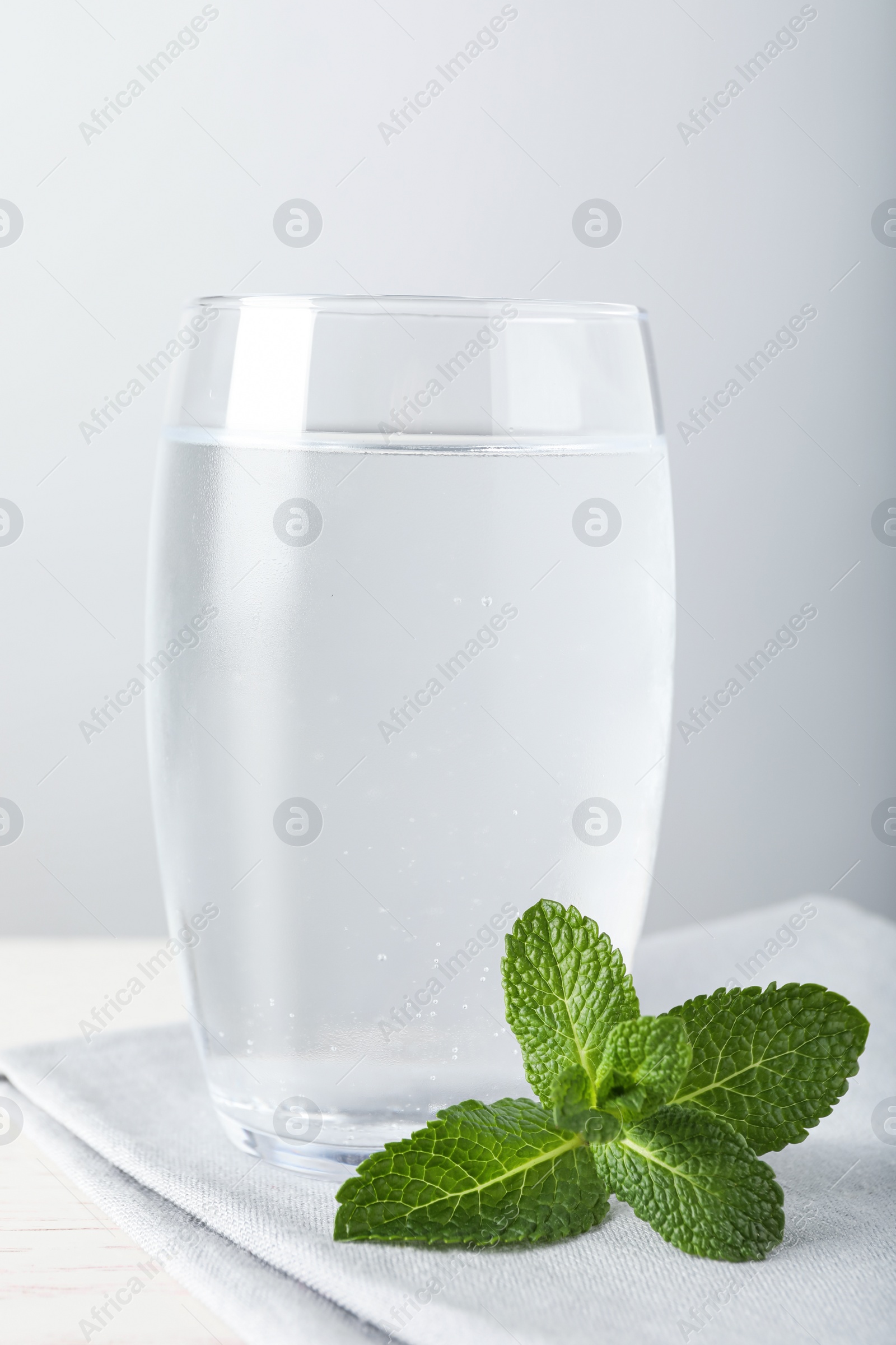 Photo of Glass of soda water, mint and napkin on white wooden table